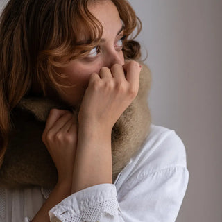 Mujer agarra con ambas manos un cuello de mohair de tejido artesano. Es suave, brillante y muy abrigado. Real Fábrica.