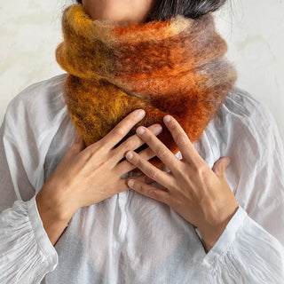 Mujer tocando con ambas manos el cuello de mohair que lleva al cuello. Tiene un diseño de tartán en tonos marrones. Real Fábrica.