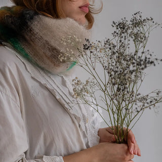 Mujer posando con un cuello de mohair con un diseño de tartán y sujetando un ramillete de flores. El cuello está confeccionado a mano por los artesanos de Ezcaray. Real Fabrica.