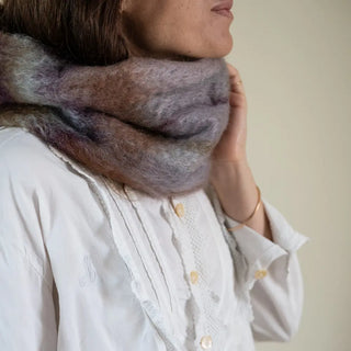 Mano de mujer agarrando el cuello de mohair morado y marrón que lleva puesto. En el primer plano se aprecia la suavidad y la calidad del tejido artesano. Real Fábrica.Fábrica.