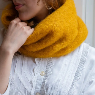 Mujer agarrando el cuello de mohair en color mostaza con el que se abriga el cuello. El mohair es suave, brillante y muy cálido. Real Fábrica.