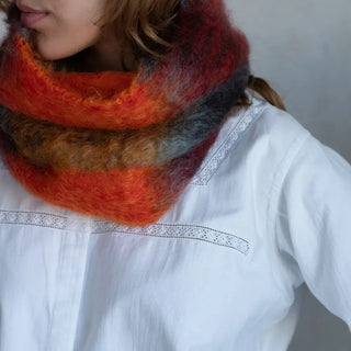 Foto de mujer abrigada con un cuello de mohair en color rojo y naranja. El mohair es brillante, suave, ligero y muy cálido. Real Fábrica.
