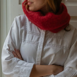 Mujer abrigada con un mullido cuello de mohair en color rojo. El mohair es una fibra de gran calidad, cálida, ligera y duradera. Real Fábrica.