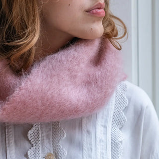 Foto de mujer abrigada con un cuello de mohair en color rosa. El mohair es brillante, suave, ligero y muy cálido. Real Fábrica.
