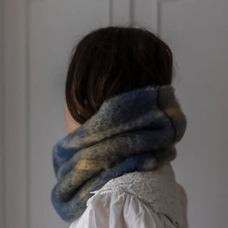Mujer de perfil abrigada con un cuello de mohair. Tiene un diseño de tartán en tonos azules. Real Fábrica.
