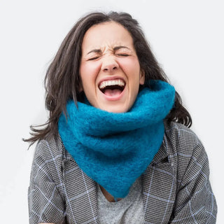 Mujer sonriente que lleva puesto un cuello hecho a mano de mohair, de color azul turquesa. Real Fábrica.
