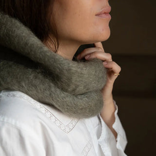 Mano de mujer agarrando el cuello de mohair verde que lleva puesto. En el primer plano se aprecia la suavidad y la calidad del tejido artesano. Real Fábrica.