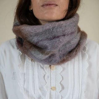 Foto de mujer abrigada con un cuello de mohair en color verde, morado y marrón. El mohair es brillante, suave, ligero y muy cálido. Real Fábrica.