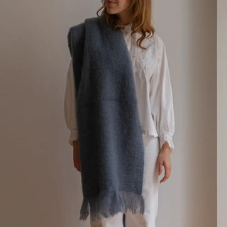 Foto de mujer luciendo nuestro Echarpe gris azulón de Ezcaray, tejido con mohair de alta calidad. Detalles de flecos cortos en los extremos y teñido manual que garantizan una pieza exclusiva y artesana. Real Fábrica.