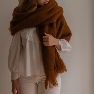 Mujer con el cuello envuelto en un echarpe en color marrón. Está confeccionado en mohair en un proceso artesanal realizado por Ezcaray, en La Rioja. Real Fábrica.