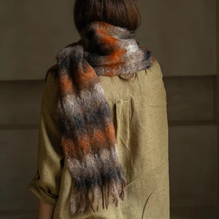 Foto de mujer de espalda luciendo un foulard de mohair con cuadros en color naranja y marrón rematado en flecos. Real Fábrica.