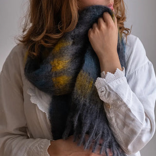 Mujer con un foulard de mohair alrededor del cuello. Tiene diseño de cuadros mostaza y azul Klein. Real Fábrica.