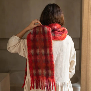 Mujer de espalda luciendo un foulard de mohair con cuadros en color naranja y rojo, rematado en flecos. Real Fábrica.
