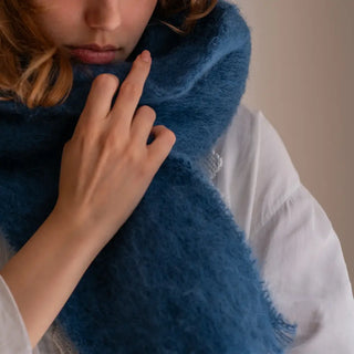 Mano de mujer tocando la suavidad de un foulard de mohair artesano de color azul. Real  Fábrica.