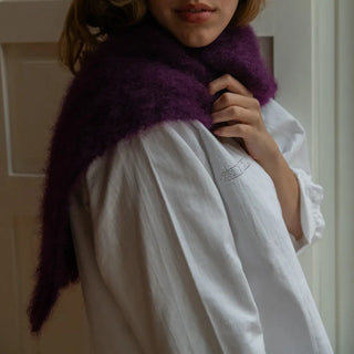 Mano de mujer acariciando la suavidad de un foulard de mohair de Ezcaray, que lleva alrededor del cuello. Es de color berenjena oscuro. Real Fábrica.