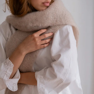 Mano de mujer sujetando el foulard de mohair en color crudo con el que se envuelve. Es cálido y muy suave. Real Fábrica.