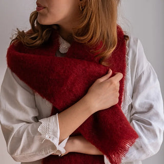 Mujer abrigada con un foulard de mohair en tono rojo oscuro, suave y muy cálido. Está confeccionado a mano por los artesanos de Ezcaray. Real Fábrica.