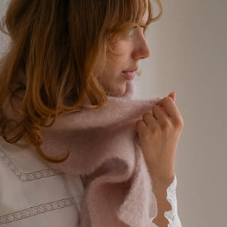 Una  mujer toca con su mano el foulard de mohair rosa palo que lleva al cuello, una fibra suave y de gran calidad desarrollada por Ezcaray, en la Rioja. Real Fábrica.