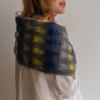 Foto de mujer de perfil abrigada con un foulard de mohair con un diseño de cuadros en amarillo y azulón. Real Fábrica