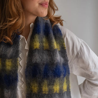 Mujer llevando un foulard de mohair con un diseño de cuadros en amarillo y azulón, artesanía tradicional española. Real Fábrica.