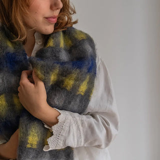 Mujer envuelta en un foulard de mohair con un diseño de cuadros. Los colores son azulón, amarillo y gris. Real Fábrica.