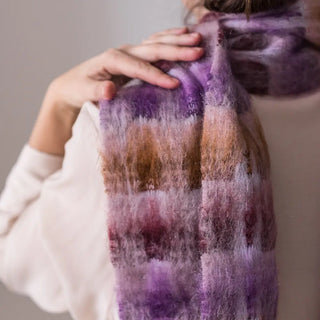 Una mujer de espalda toca con su mano el foulard de mohair de cuadros morados y ocres que lleva al cuello, una fibra suave y de gran calidad desarrollada por Ezcaray, en la Rioja. Real Fábrica.