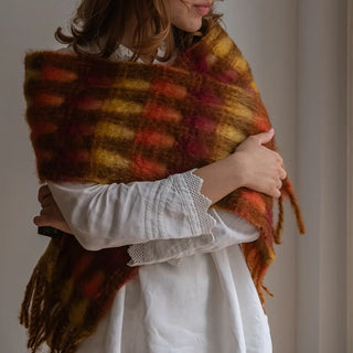 Foto de mujer envuelta en un foulard de mohair de cuadros rojos y amarillos. Está rematado en suaves flecos. Real 
