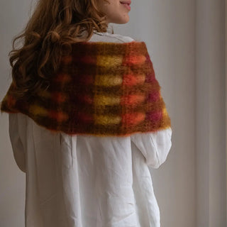 Mujer de espalda abrigada con un foulard de mohair de cuadros rojos y amarillos. Está fabricado a mano por artesanos de La Rioja. Real Fábrica.