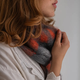 Mujer tocando un suave y abrigado  foulard de mohair con cuadros en tonos rojos, hecho a mano en La Rioja. Real Fábrica.