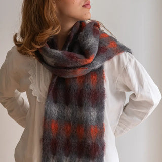 Foto de mujer luciendo nuestro foulard de mohair con cuadros en tonos rojos. Está hecho artesanalmente en La Rioja. Real Fábrica.