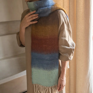 Mujer abrigada con un foulard de mohair de franjas azul, mostaza y blanco, una fibra de origen natural ultra cálida y ligera, de gran calidad. Real Fábrica. 