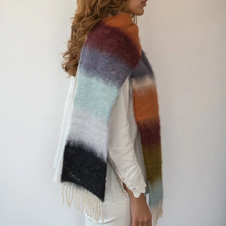 Foto de mujer de perfil abrigada con un suave y cálido foulard de franjas berenjena, caldera y gris perla. Real Fábrica.