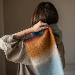 Mujer envuelta en un foulard bufanda de mohair en 3 colores: naranja, azul y mostaza. El tejido artesano es de gran calidad, suave y muy cálido. Real Fábrica.