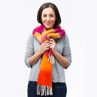 Mujer abrigada con un foulard de mohair de franjas naranja, con sus dos manos toca una fibra de origen natural ultra cálida y ligera, de gran calidad. Real Fábrica. 