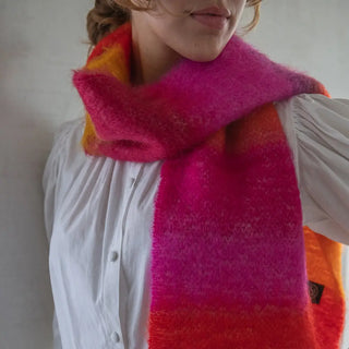 Una mujer luciendo un foulard de mohair de franjas naranja y rosa que lleva al cuello, una fibra suave y de gran calidad desarrollada por Ezcaray, en la Rioja. Real Fábrica.