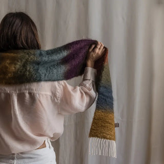 Una mujer de espalda toca con su mano el foulard de mohair de franjas oscuras que lleva al cuello, una fibra suave y de gran calidad desarrollada por Ezcaray, en la Rioja. Real Fábrica.