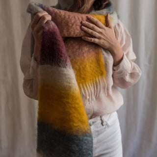 Foto de mujer abrigada un foulard de mohair de franjas pastel, tejido a mano por los artesanos de Ezcaray. Real Fábrica.