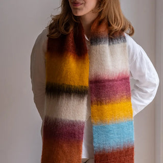 Foto de mujer luciendo un foulard de mohair de franjas terracota, mostaza y blanco sobre los hombros. Real Fábrica.
