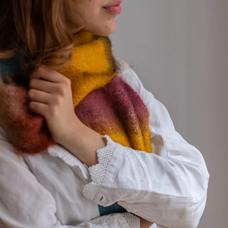 Mano de mujer agarrando un foulard de mohair de franjas terracota, mostaza y blanco, cálido y suave. Real Fábrica.