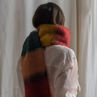 Foto de mujer de espalda abrigada con un foulard de mohair de rayas verdes, una fibra de origen natural ultra cálida y ligera, de gran calidad. Real Fábrica. 