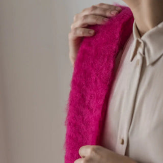 Una mujer toca con su mano el foulard de mohair fucsia que lleva en uno de sus hombros, una fibra suave y de gran calidad desarrollada por Ezcaray, en la Rioja. Real Fábrica.