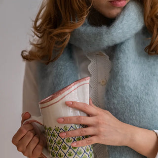 Mujer sujetando una jarra de cerámica de Cáceres y con un foulard de mohair gris celeste alrededor del cuello. Productos artesanos españoles. Real Fábrica.