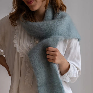 Mujer con un foulard de mohair gris celeste alrededor del cuello. La fibra de mohair es suave y muy cálida. Real Fábrica.