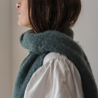 Foto de mujer de perfil luciendo un foulard de mohair, suave, cálido y ligero. Está hecho a mano por los artesanos riojanos de Ezcaray. Real Fábrica