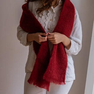 Mujer posando con un foulard de mohair rojo oscuro sobre los hombros. Terminaciones en flecos finos. Real Fábrica.