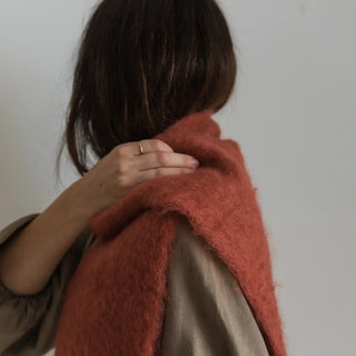 Una mujer toca con su mano el foulard de mohair rosa terracota que lleva al cuello, una fibra suave y de gran calidad desarrollada por Ezcaray, en la Rioja. Real Fábrica.