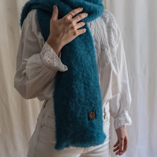 Mujer abrigada con un foulard de mohair turquesa, una fibra de origen natural ultra cálida y ligera, de gran calidad. Real Fábrica. 
