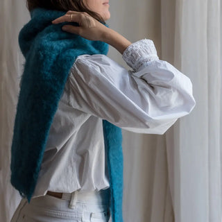Una mujer de perfil toca con su mano el foulard de mohair turquesa que lleva al cuello, una fibra suave y de gran calidad desarrollada por Ezcaray, en la Rioja. Real Fábrica.