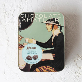 Foto de lata estilo Art Decó con hojas de cacao 70% flor de sal. Lata cerrada sobre superficie blanca. Real Fábrica. 