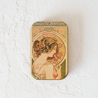 Foto de una lata de hojas de chocolate con leche cerrada sobre una superficie blanca. Real Fábrica.